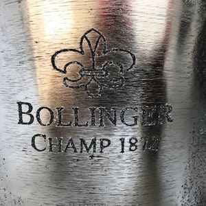 May include: A silver champagne bucket with the Bollinger logo and the text "Champ 1872" engraved on the front.