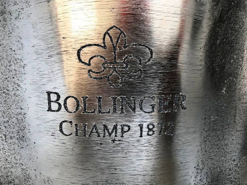 May include: A silver champagne bucket with the Bollinger logo and the text "Champ 1872" engraved on the front.
