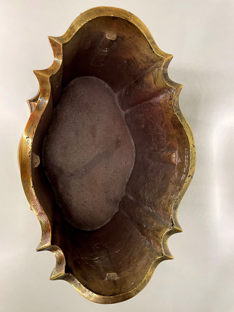 May include: A brass planter with a scalloped edge and a worn, aged finish. The planter is empty and ready for planting.