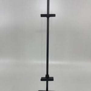May include: A black metal display stand with a square base, a vertical pole, and two horizontal crossbars. The stand is designed to hold items for display. The stand is made of metal and has a matte finish.