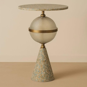 Puede incluir: Una mesa auxiliar decorativa con una tapa redonda y una base estampada. La mesa presenta un globo transparente y texturizado en el centro, acentuado con metal dorado. La base tiene forma de cono con un patrón azul y dorado.