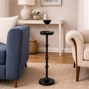 May include: A black metal wine glass holder with a round base and a small tray. A wine glass filled with red wine sits on the tray. The holder is next to a blue sofa and a cream armchair.