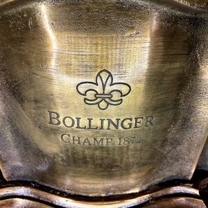 May include: A gold-colored metal plaque with a fleur-de-lis design and the text "Bollinger Champ 1872".