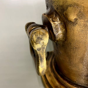 May include: A close-up of a brass ice bucket with a handle. The bucket has a textured surface and a decorative base.