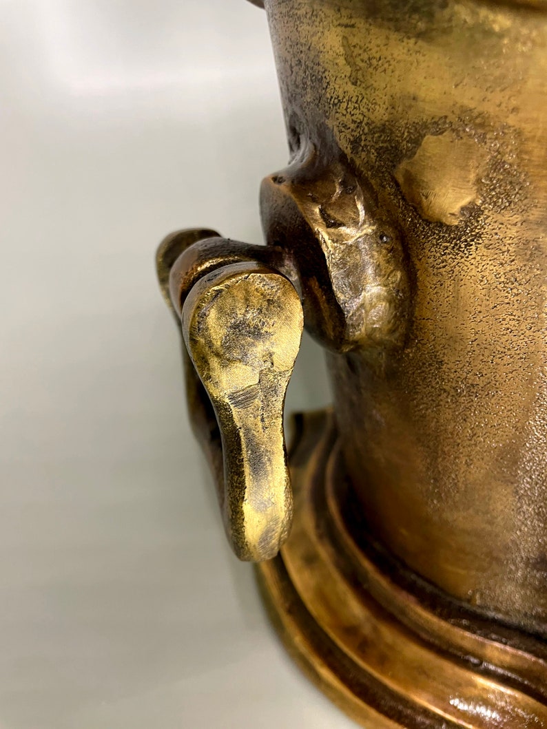 May include: A close-up of a brass ice bucket with a handle. The bucket has a textured surface and a decorative base.