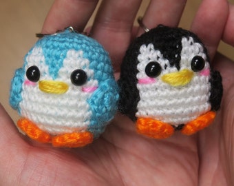 May include: Two crocheted penguin keychains, one blue and one black, with white faces, orange beaks, and black eyes.