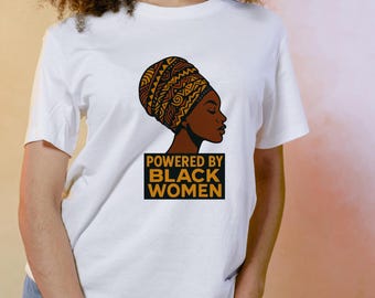 Puede incluir: Camiseta blanca con un gráfico de una mujer negra con un pañuelo en la cabeza estampado. El texto "POWERED BY BLACK WOMEN" se muestra debajo del gráfico en un rectángulo negro y dorado.