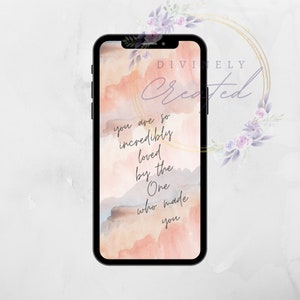 May include: A phone screen with a watercolour background in shades of pink and blue. The text "Divinely Created" is written in gold script at the top of the screen. The text "You are so incredibly loved by the One who made you" is written in black script on the screen.