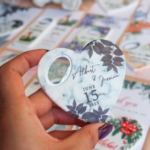 Peut inclure: D&eacute;capsuleur en forme de c&oelig;ur avec un motif marbr&eacute;, portant les noms "Albert & Jessica" et la date "15 juin 2025". Le d&eacute;capsuleur pr&eacute;sente un motif de feuilles florales et une ouverture circulaire. Cadeaux de mariage.