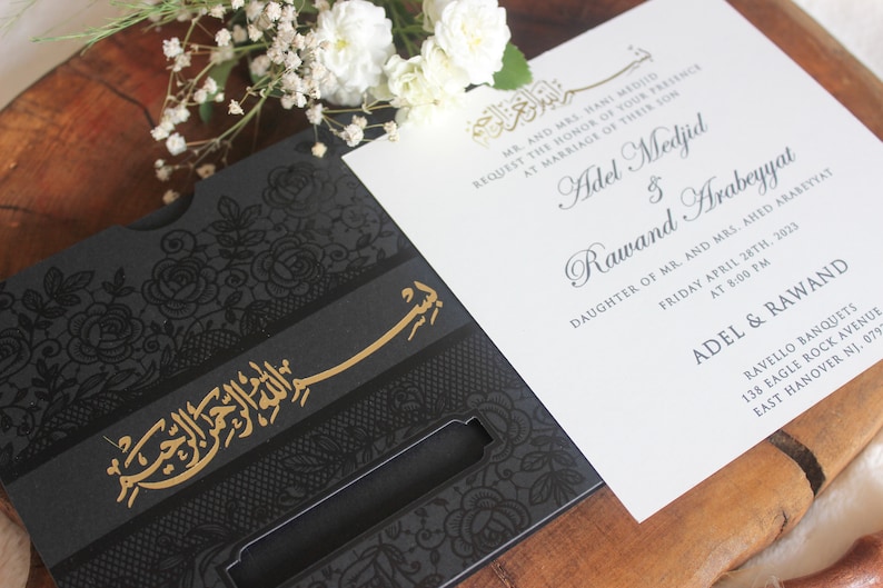 K&ouml;nnte beinhalten: Eine schwarze und goldene Hochzeitseinladung mit einem filigranen Blumendesign und arabischer Kalligraphie. Die Einladung lautet "Adel Medjid & Rawand Arabeyyat" und enth&auml;lt Datum und Uhrzeit der Hochzeitszeremonie. Die Einladung liegt auf einer Holzoberfl&auml;che mit wei&szlig;en Blumen.