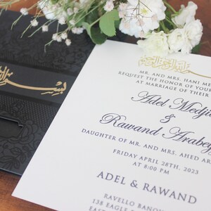K&ouml;nnte beinhalten: Eine wei&szlig;e Hochzeitseinladung mit schwarzer und goldener Kalligraphie. Die Einladung verk&uuml;ndet die Hochzeit von Adel Medjid und Rawand Arabeyyat am Freitag, den 28. April 2023 um 20:00 Uhr.
