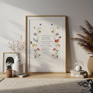 May include: A framed print with floral and butterfly illustrations and the text of Romans 8:11. The artwork has a light wooden frame and is displayed on a light-coloured wall. The floral arrangement includes red, yellow, and white flowers.
