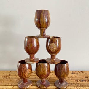 May include: Set of six brown and orange marble wine glasses with a stemmed base. The glasses are stacked in a pyramid shape.