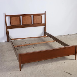 May include: A mid-century modern bed frame with a headboard featuring three woven cane panels. The frame is constructed of dark wood and has a low-profile design. The bed frame is designed to accommodate a standard mattress.