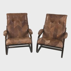 May include: Two vintage armchairs with high backs. The chairs feature brown leather upholstery in a patchwork design. The wooden frames are dark brown, and the armrests are padded. The chairs are set against a white background.