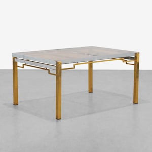 May include: Rectangular table with a glass top and a metal frame. The frame features gold-colored legs and a silver-colored border around the glass. The table's design is geometric and modern, suitable for a living room or dining area.