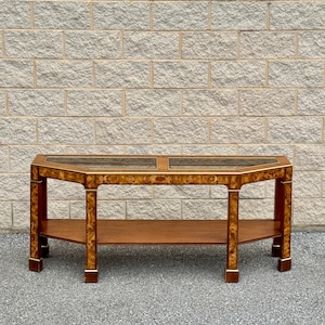 May include: A long, rectangular console table with a wood veneer top and a lower shelf. The table has a beveled edge and a glass top. The table is made of wood and has a dark brown finish.
