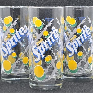 Könnte beinhalten: Drei transparente Sprite-Gläser mit dem Sprite-Logo in Blau und Weiß, gelben Zitronen und einem grauen Gittermuster. Die Gläser sind hoch und zylindrisch, ideal zum Servieren von kalten Getränken.