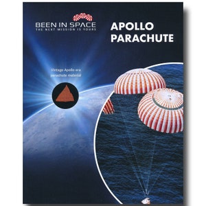 Op de afbeelding: Een rood, wit en blauwe Apollo-tijdperk parachute met de tekst "BEEN IN SPACE THE NEXT MISSION IS YOURS" en "APOLLO PARACHUTE" op een blauwe achtergrond met een vintage Apollo-tijdperk parachute materiaalmonster.
