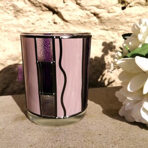 May include: A pink glass candle holder with a stained glass design featuring purple and black geometric shapes.