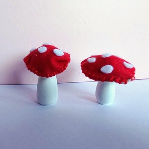 May include: Two red felt mushrooms with white polka dots on top of white wooden bases.