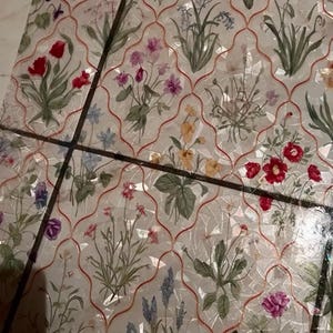 May include: A decorative surface with a floral design. The pattern showcases flowers in red, pink, purple, and yellow, set against a white backdrop with a red lattice overlay. The surface is divided into sections by dark lines, creating a mosaic effect.