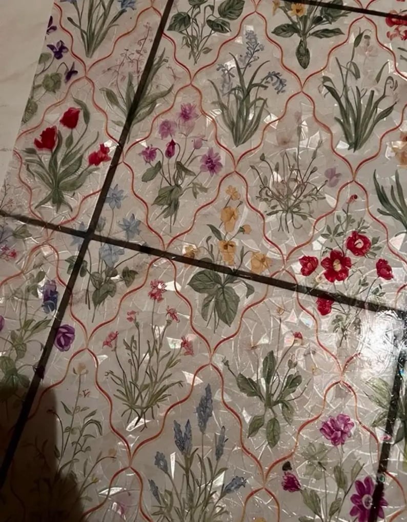 May include: A decorative surface with a floral design. The pattern showcases flowers in red, pink, purple, and yellow, set against a white backdrop with a red lattice overlay. The surface is divided into sections by dark lines, creating a mosaic effect.