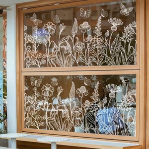 Peut inclure: Une fenêtre à cadre en bois ornée d'un motif floral et de papillons blancs gravé sur le verre. Le motif comprend diverses fleurs, feuilles et papillons, créant une esthétique inspirée de la nature. La fenêtre est divisée en deux sections.
