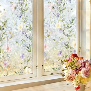 May include: Window film with a floral design in watercolour style. The film features pink, purple, and yellow flowers with green leaves and vines. The window has a white frame. A bouquet of flowers sits on the windowsill.