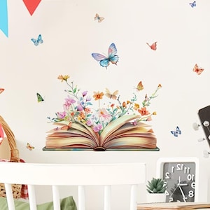 May include: A wall decal featuring an open book with colorful flowers and butterflies. The book's pages are a warm yellow, and the flowers include pink, orange, and yellow blooms. Several butterflies in various colors are scattered around the book.