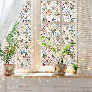 May include: A window with a floral design, showcasing a range of colourful flowers and green leaves on a white backdrop. The window is framed in white, with a wooden sill and potted plants. Sunlight creates a rainbow effect.