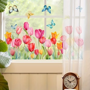 May include: A window with a floral design featuring colorful tulips in shades of pink, red, and yellow, with green leaves. Butterflies in various colors are also depicted. A sheer white curtain is visible on the right side of the window. A wooden clock is in the foreground.
