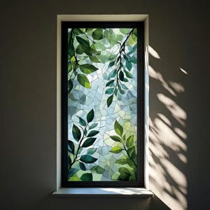 Könnte beinhalten: Ein rechteckiges Fenster mit schwarzem Rahmen zeigt ein Buntglasdesign mit grünen Blättern und einem Mosaikhintergrund. Die Blätter sind in verschiedenen Grüntönen gehalten, und der Hintergrund ist eine Mischung aus hellen Blau- und Grüntönen.