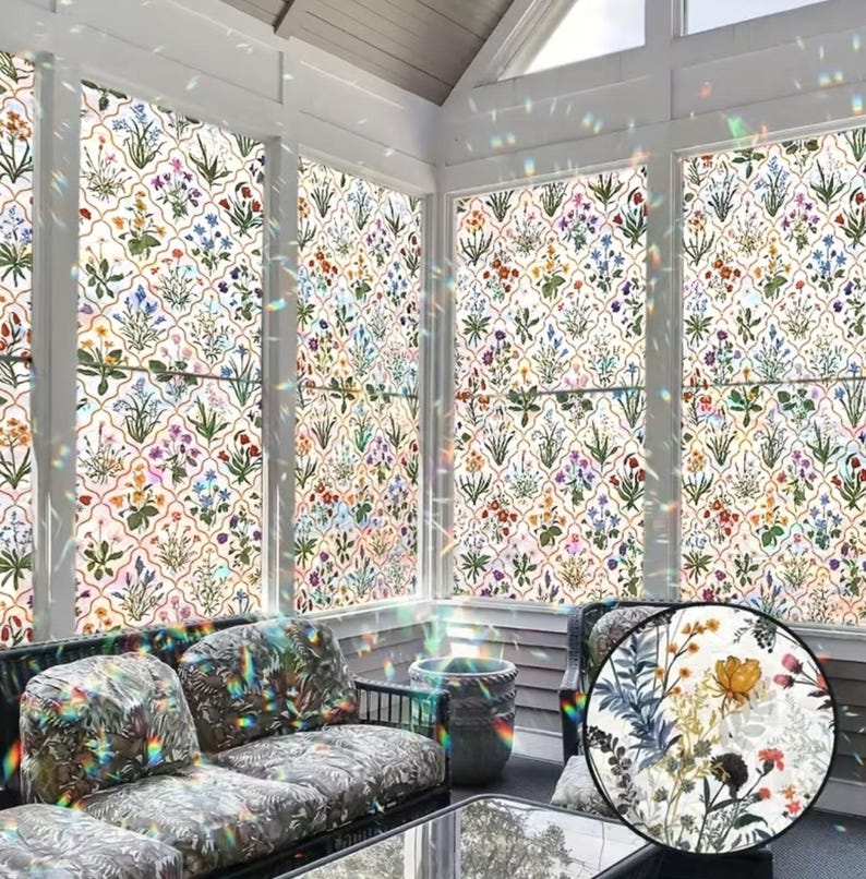 May include: A conservatory with windows adorned with floral patterned window film. The film displays a repeating pattern of colourful flowers and foliage on a white backdrop. The room features a sofa with patterned cushions and a glass-topped table.