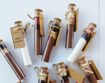 May include: Ten glass test tubes with cork tops filled with different ingredients, including chocolate powder, sprinkles, and white chocolate. Each tube is tied with twine and a small brown paper tag.