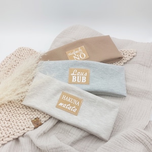 Könnte beinhalten: Drei graue und beige gestreifte Stoff-Stirnbänder mit braunen Leder-Patches. Die Patches haben weißen Text, der "einfach NO", "Laus BUB" und "HAKUNA matata" lautet.