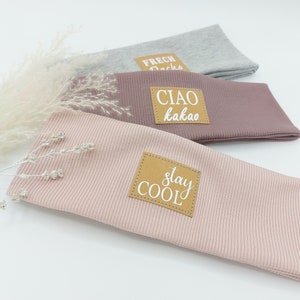 May include: Three fabric headbands with different colors and phrases. The top headband is gray with the phrase "Frech Dachs". The middle headband is pink with the phrase "Ciao kakao". The bottom headband is light pink with the phrase "Stay Cool".