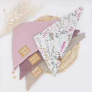 May include: Three fabric bandanas with different patterns and colors. The top bandana is white with a floral pattern, the middle bandana is pink, and the bottom bandana is beige. Each bandana has a brown leather patch with white text. The top bandana says "Hakuna Matata", the middle bandana says "Einfach No", and the bottom bandana says "Dorf Kind".