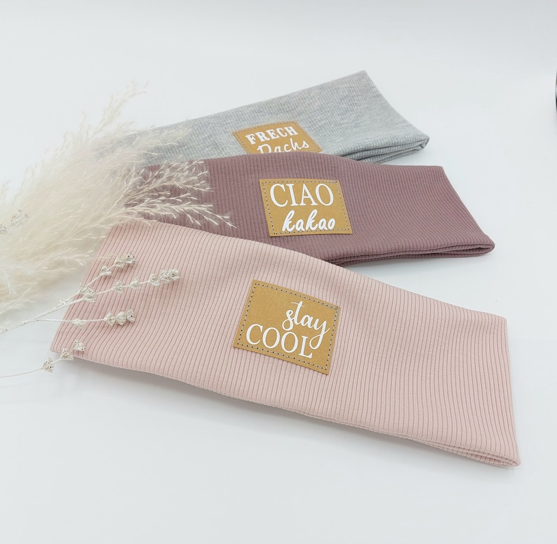 May include: Three fabric headbands with different colors and text on brown patches. The top headband is gray with the text "FRECH DACHs". The middle headband is pink with the text "CIAO kakao". The bottom headband is light pink with the text "stay COOL".