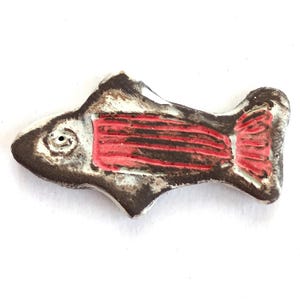 May include: A ceramic fish figurine with a dark brown body, white accents, and red detailing. The fish has a stylized design with visible gills and internal structure. The figurine is likely handmade and suitable for home decor.