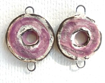 May include: Two circular ceramic components featuring a central hole, a textured white and dark brown outer rim, and a vibrant pink marbled interior surface. Each piece includes two small silver-toned metal loops attached at the top and bottom.
