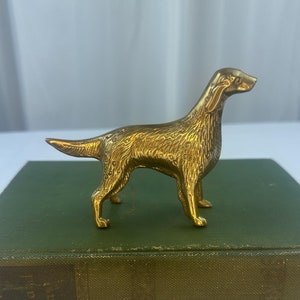 May include: A gold-colored brass figurine of a dog, possibly a pointer, standing on a green book. The book has the title "Nine Plays" by Bernard Shaw.