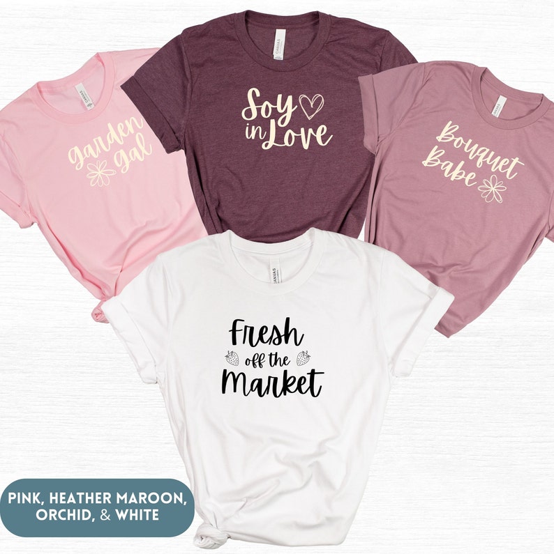 May include: Four t-shirts with different designs and colors. The shirts are pink, heather maroon, orchid, and white. The designs include "garden gal", "Soy in Love", "Bouquet Babe", and "Fresh off the Market".