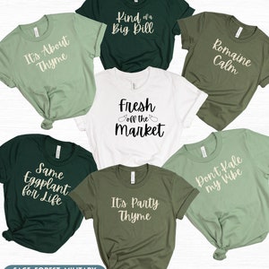 May include: Six different t-shirts with various vegetable puns. The shirts are in sage, forest, military green, and white colors. The text on the shirts reads: "It's About Thyme", "Kind of a Big Dill", "Romaine Calm", "Fresh Off the Market", "Same Eggplant for Life", "It's Party Thyme", and "Don't Kale My Vibe".