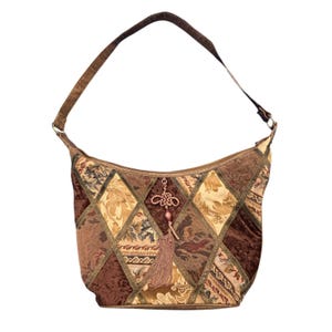 May include: A hobo-style shoulder bag featuring a patchwork design of brown, tan, and gold fabric panels. The bag includes a single shoulder strap and a decorative hanging ornament with a knotted cord and a long, light brown fabric tassel.
