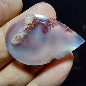 Peut inclure: Un cabochon d'agate en forme de larme avec une base blanche et des inclusions dendritiques brunes et rouges.