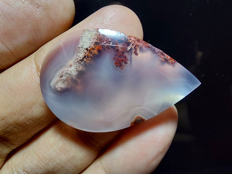 Peut inclure: Un cabochon d'agate en forme de larme avec une base blanche et des inclusions dendritiques brunes et rouges.
