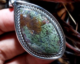 May include: A teardrop-shaped pendant with a green and brown agate stone set in a silver bezel with a rope design.