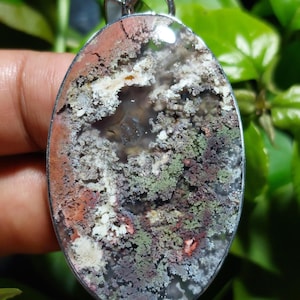 Può includere: Un ciondolo d'argento con una grande pietra di agata di forma ovale che presenta un motivo dendritico unico. La pietra è un mix di colori bianchi, grigi, verdi e marroni.