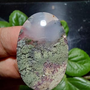 May include: A green, white, and pink agate cabochon with a mossy pattern. The cabochon is oval shaped and has a smooth, polished surface.